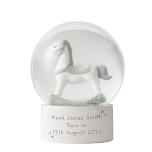 May include: A snow globe with a white base and a clear glass dome. Inside, a white and grey rocking horse is visible. The base is inscribed with the text "Noah James Smith Born on 13th August 2022".