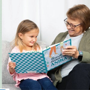 May include: A grandmother and granddaughter are reading a personalized book together. The book cover is blue and white checkered with the text "Grandma Janice loves Anika".