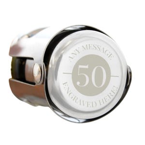May include: A silver champagne bottle stopper with a circular face. The face has the number "50" in a light grey circle, with the words "ANY MESSAGE ENGRAVED HERE!" around the edge.
