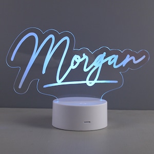 May include: A white acrylic night light with the name "Morgan" written in a cursive font. The light is on and emitting a blue glow.