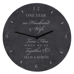 May include: A black slate clock with white text that reads "One Year as Husband & Wife Time Flies When We're Together Ellie & Keiron".
