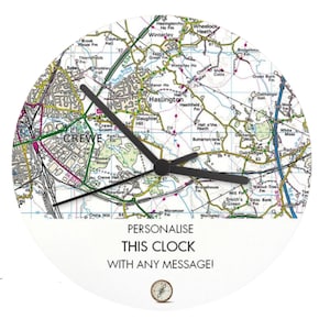 May include: Circular wall clock with a map design, black hands, and the text "PERSONALISE THIS CLOCK WITH ANY MESSAGE!". The clock face shows a detailed map of a local area. A small compass graphic is also present.