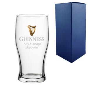 May include: A clear pint glass featuring the Guinness logo and the text "Guinness, Any Message, Any Font" in silver. A gold harp emblem is above the word Guinness. A blue gift box is to the right.