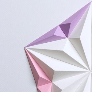 May include: Geometric paper art piece featuring a starburst design. The artwork uses white, light pink, and lavender paper, creating a three-dimensional effect. The paper is folded into sharp angles and shapes, with a clean, modern aesthetic.