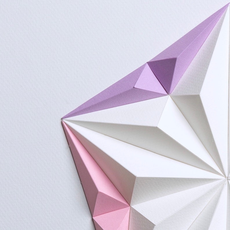 May include: Geometric paper art piece featuring a starburst design. The artwork uses white, light pink, and lavender paper, creating a three-dimensional effect. The paper is folded into sharp angles and shapes, with a clean, modern aesthetic.