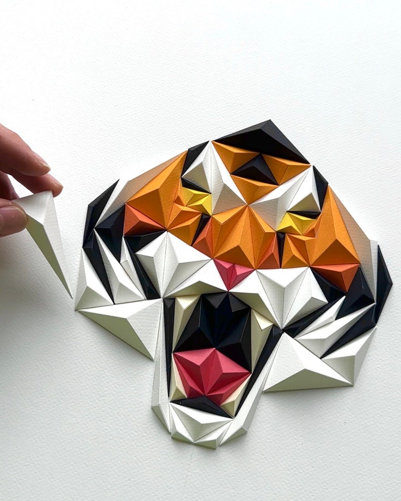 Puede incluir: Una escultura de tigre de papel con un esquema de color blanco, naranja, negro y rojo. La boca del tigre est&aacute; abierta, mostrando sus dientes. La escultura est&aacute; hecha de muchos tri&aacute;ngulos peque&ntilde;os.