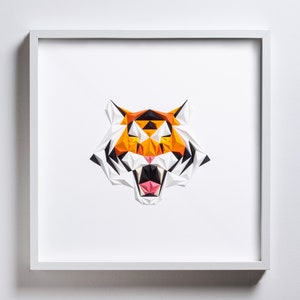 Puede incluir: Una impresi&oacute;n enmarcada en blanco de una cabeza de tigre geom&eacute;trica con papel naranja, negro y blanco.