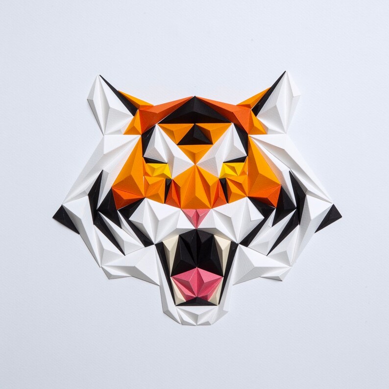 Puede incluir: Una escultura de cabeza de tigre de papel con formas geom&eacute;tricas naranja, blanca y negra. La boca del tigre est&aacute; abierta y se ven sus dientes.