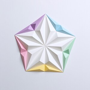 May include: A geometric paper art piece in the shape of a five-pointed star. The star is composed of white, pastel pink, yellow, green, light blue, and purple paper. The star's design features a series of folded, triangular facets.