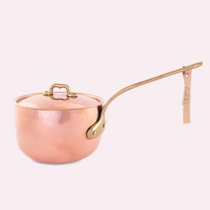 May include: A hammered copper saucepan with a long brass handle and lid. The saucepan has a brass tag attached to the handle that reads "NAVARINI - CUDINI ITALY".