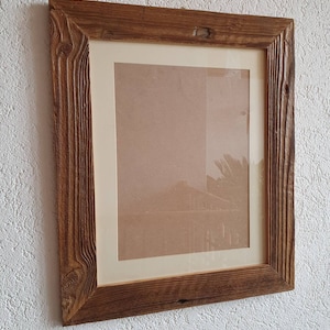May include: A rustic wooden picture frame with a natural brown finish. The frame has a thick, textured border and a simple, rectangular shape.