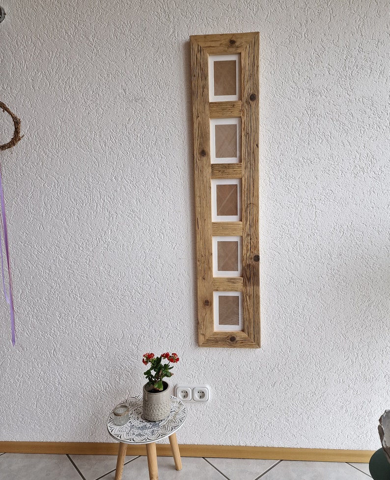 Pu&ograve; includere: Una cornice per foto in legno rustico con cinque aperture per foto. La cornice &egrave; realizzata in legno riciclato e ha una finitura naturale. La cornice &egrave; appesa a una parete bianca.