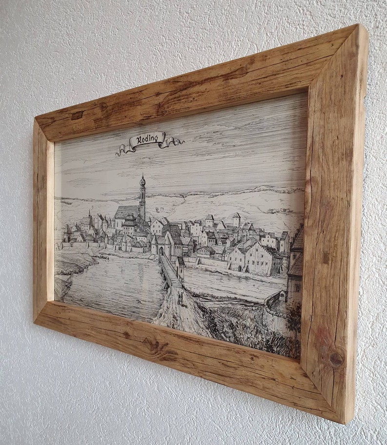 Puede incluir: Un dibujo en blanco y negro enmarcado de una ciudad hist&oacute;rica con la palabra "Roding" en una pancarta en la parte superior. El dibujo representa una ciudad con un r&iacute;o que la atraviesa y una iglesia con un alto campanario en el centro.
