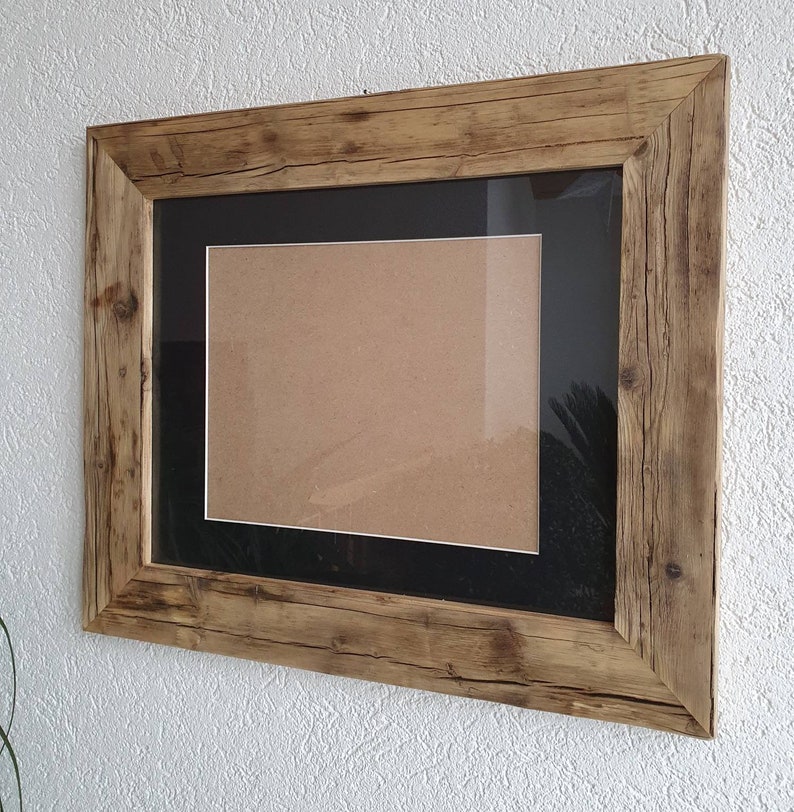 Puede incluir: Un marco de fotos de madera r&uacute;stica con un passe-partout negro y un inserto de cart&oacute;n marr&oacute;n. El marco tiene un acabado de madera natural y est&aacute; hecho de madera reciclada.