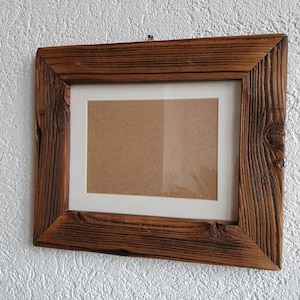 May include: A rustic wooden picture frame with a brown stain and a white mat. The frame has a simple design and is perfect for displaying photos or artwork.