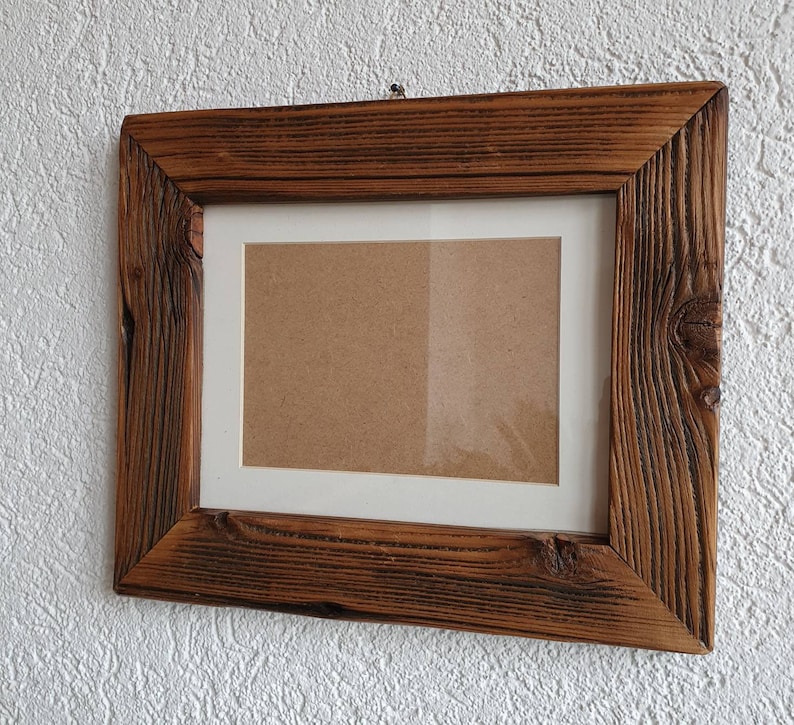 May include: A rustic wooden picture frame with a brown stain and a white mat. The frame has a simple design and is perfect for displaying photos or artwork.