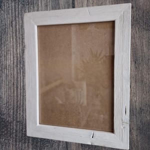 Puede incluir: Marco de fotos de madera blanca con un paspart&uacute; marr&oacute;n claro. El marco tiene un aspecto r&uacute;stico y desgastado.