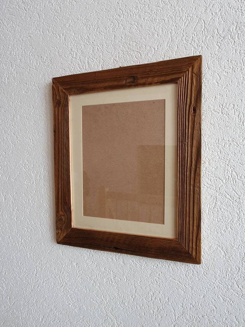 May include: A rustic wooden picture frame with a light brown wood finish. The frame has a white mat and is hanging on a white textured wall.