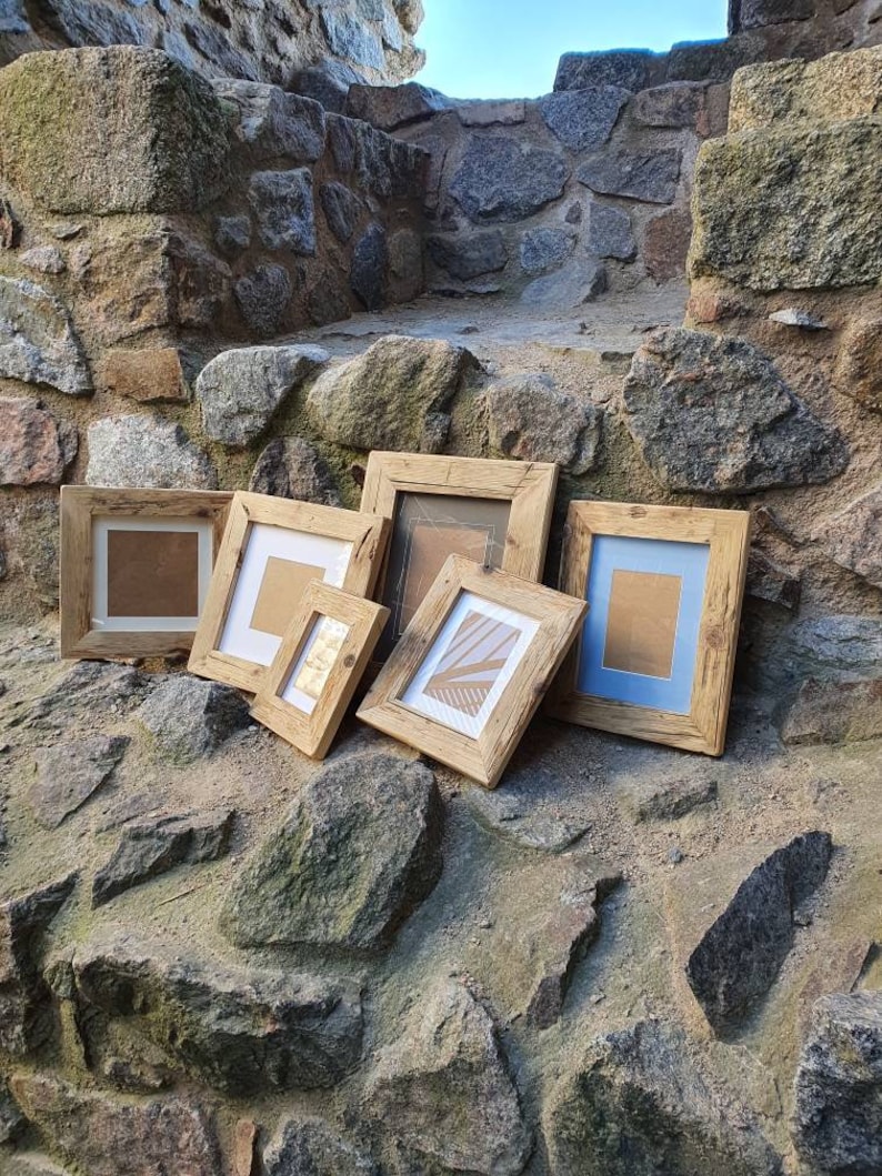 Puede incluir: Seis marcos de fotos de madera r&uacute;stica de diferentes tama&ntilde;os, dispuestos sobre una superficie de piedra. Los marcos son todos de madera natural con un aspecto tosco y sin terminar. Algunos marcos tienen un acabado marr&oacute;n claro, mientras que otros tienen un acabado marr&oacute;n oscuro. Los marcos est&aacute;n todos vac&iacute;os y listos para ser rellenados con fotos u obras de arte.