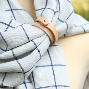 May include: A light blue and white plaid scarf with a brown leather scarf holder.