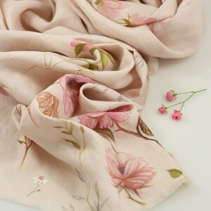 May include: A soft, blush-colored scarf with a delicate floral print. The scarf is made of a lightweight fabric and has a fringed edge.