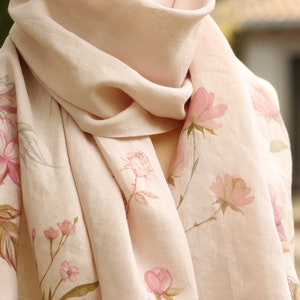 May include: A pale pink linen scarf with a floral print of pink flowers and green leaves.
