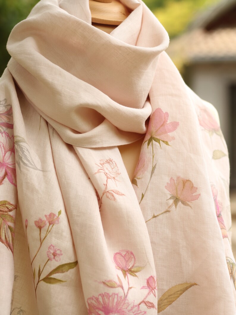 May include: A pale pink linen scarf with a floral print of pink flowers and green leaves.