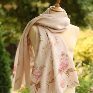 May include: A pale pink scarf with a floral print featuring pink flowers and green leaves. The scarf is draped over a white mannequin.