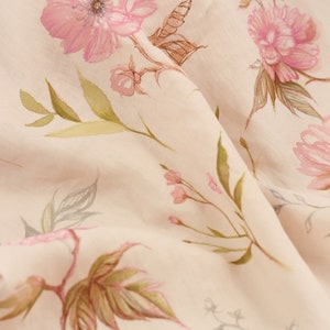 May include: A close-up of a pale pink fabric with a delicate floral pattern. The flowers are pink and white with green leaves. The fabric is soft and flowing.