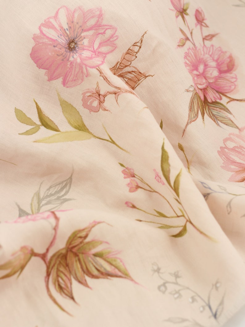 May include: A close-up of a pale pink fabric with a delicate floral pattern. The flowers are pink and white with green leaves. The fabric is soft and flowing.