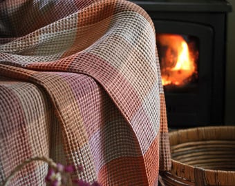 May include: A waffle-weave throw blanket featuring a large-scale plaid pattern in shades of burnt orange, muted brown, cream, and soft mauve. The fabric has a distinct grid-like texture and is draped over a piece of furniture, showing its thickness.