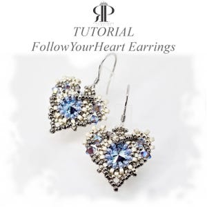 May include: A pair of heart-shaped beaded earrings featuring a central blue crystal, surrounded by metallic grey and cream-colored seed beads. The text TUTORIAL FollowYourHeart Earrings is visible above the jewelry with a logo at the top.