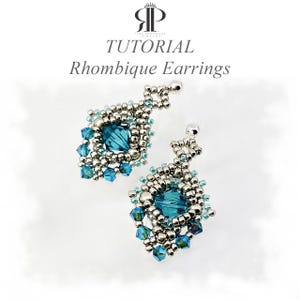 May include: A pair of beaded earrings featuring a central dark teal crystal surrounded by metallic silver seed beads and smaller light blue crystal accents. The text TUTORIAL Rhombique Earrings is displayed above the jewelry pieces.