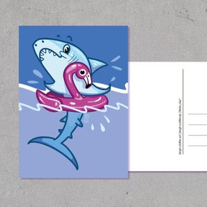 May include: A postcard with a cartoon shark wearing a pink flamingo inflatable ring in blue water. The shark is light blue with white details and a wide grin. The postcard's back is white with lines for writing and a stamp.