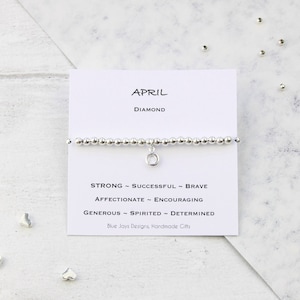 May include: A silver bracelet with a charm that says "April" and "Diamond". The bracelet also has a card with the text "Strong ~ Successful ~ Brave ~ Affectionate ~ Encouraging ~ Generous ~ Spirited ~ Determined" and "Blue Jays Designs, Handmade Gifts".