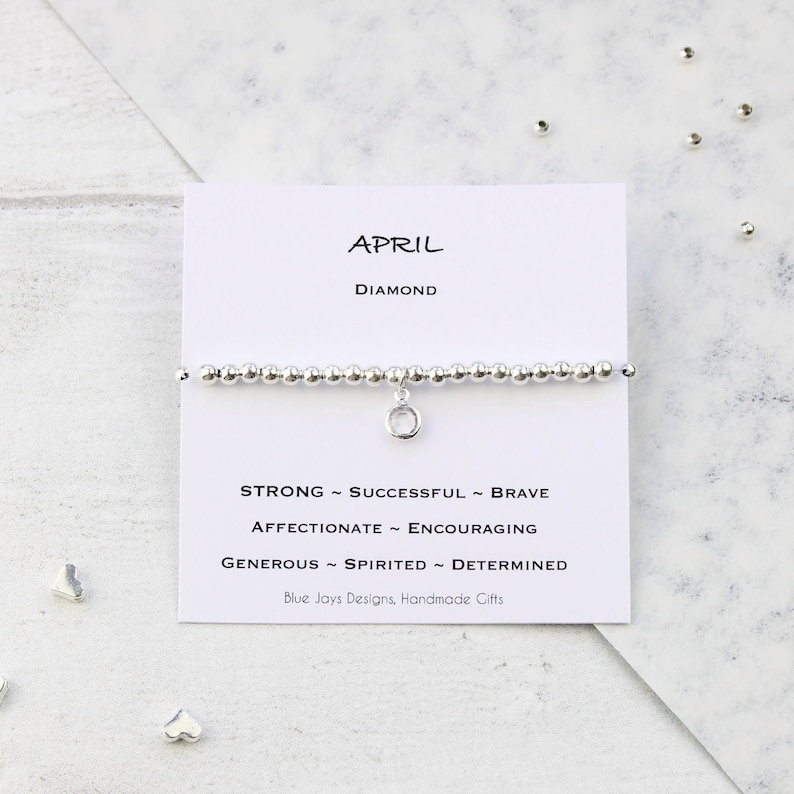 May include: A silver bracelet with a charm that says "April" and "Diamond". The bracelet also has a card with the text "Strong ~ Successful ~ Brave ~ Affectionate ~ Encouraging ~ Generous ~ Spirited ~ Determined" and "Blue Jays Designs, Handmade Gifts".