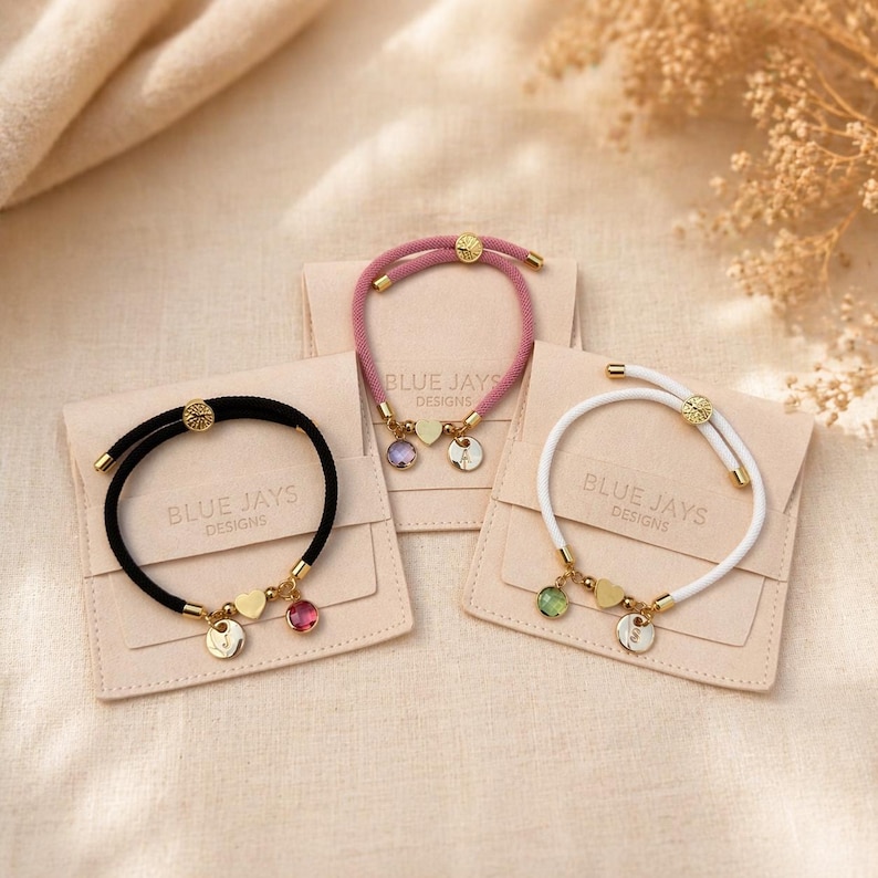 Pink, white and black personalised heart bracelets with initial charms and birthstones on gift pouches
