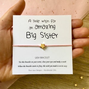 May include: A pink wish bracelet with a gold star charm and a card that reads "A little wish for an amazing Big Sister". The card also includes instructions for making a wish and the text "Wish Bracelet".