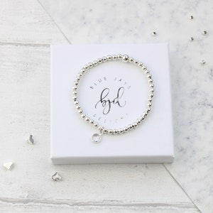 May include: A silver bracelet with a clear crystal charm. The bracelet is in a white box with the text "Blue Jays byd Designs" on it.
