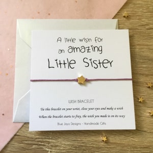 May include: A white card with the text "A little wish for an amazing Little Sister" and a purple string bracelet with a gold star charm. The card also includes the text "WISH BRACELET" and instructions for making a wish.