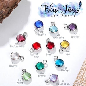 May include: Twelve silver charms with colored gemstones, each representing a different month of the year. The charms are arranged in a circle, with the month name and gemstone name written below each charm. The charms are perfect for adding a personal touch to jewelry.