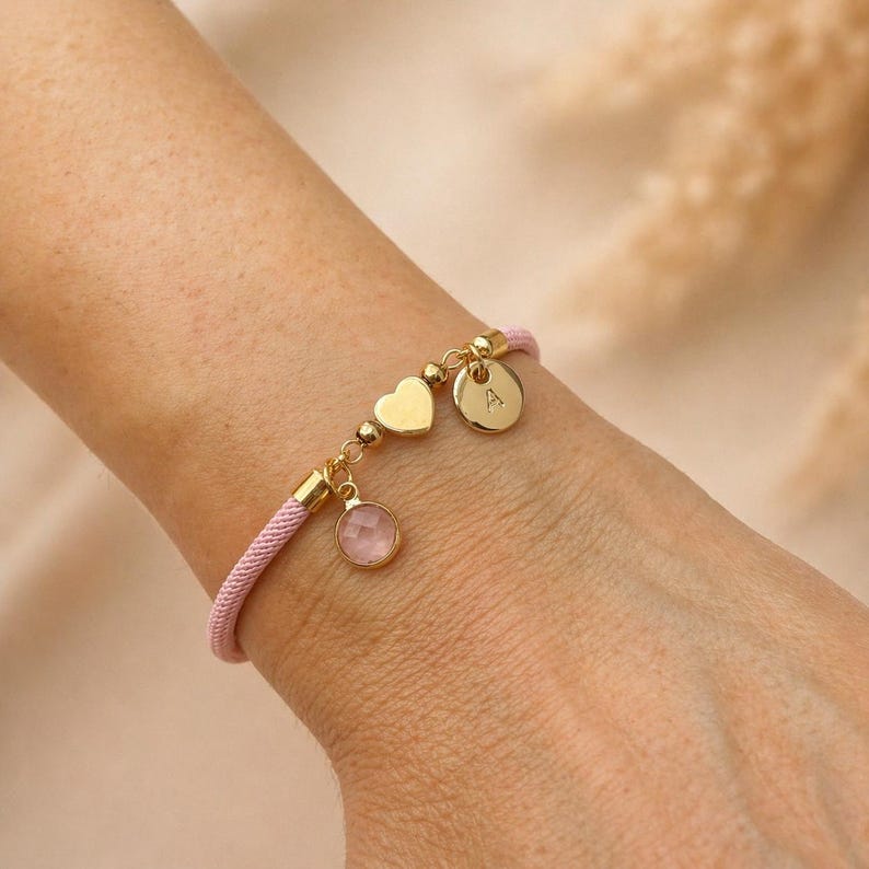 Pink personalised heart bracelet worn on wrist with gold initial charm and birthstone, gift for girls