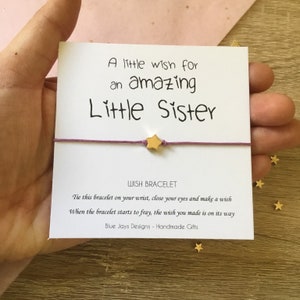 May include: A purple wish bracelet with a gold star charm and a card that reads "A little wish for an amazing Little Sister". The card also includes instructions for making a wish and the text "Blue Jays Designs - Handmade Gifts".