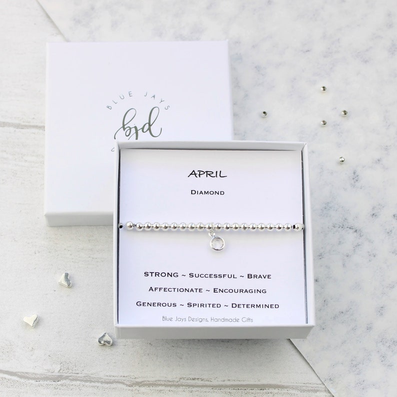May include: A silver bracelet with a charm that says "April" and "Diamond". The bracelet is in a white box with the words "Blue Jays Designs, Handmade Gifts".