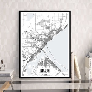 Pode incluir: Uma impressão emoldurada em preto e branco do mapa de Duluth, Minnesota, EUA. O mapa mostra o layout da cidade com estradas, edifícios e a costa do Lago Superior. A impressão é exibida em uma mesa de vidro com livros e uma planta.