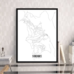 May include: A framed black and white print of a topographical map of Sundance, Utah, USA. The print is displayed on a glass table with books, a small plant, and a decorative stamp.