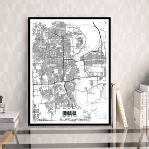 Puede incluir: Impresión enmarcada en blanco y negro del mapa de Omaha, Nebraska, EE. UU. El mapa detallado de la ciudad presenta calles, vías fluviales y el nombre de la ciudad en negrita. La impresión se muestra en una pared clara, con libros y una planta.