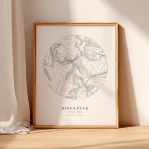 Può includere: Una stampa incorniciata con una mappa topografica circolare di Kings Peak, Utah, USA. La mappa è in bianco e nero, con linee di contorno. Include il testo "KINGS PEAK" e dettagli sull'altitudine. La cornice è in legno chiaro.