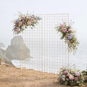 Könnte beinhalten: Zwei goldfarbene Metallgitter-Hintergründe, verziert mit pastellfarbenen Blumen, vor einer Küstenkulisse. Ein kleines Blumenarrangement befindet sich am Boden. Ideal für Hochzeiten oder Veranstaltungen.