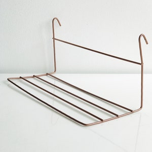 May include: A copper-colored metal shelf with hooks on either end. The shelf has four horizontal bars for support.